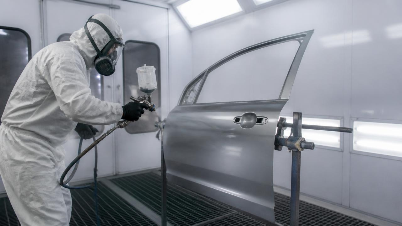 Auto painter spraying clear coat on a single car door panel inside a paint booth
