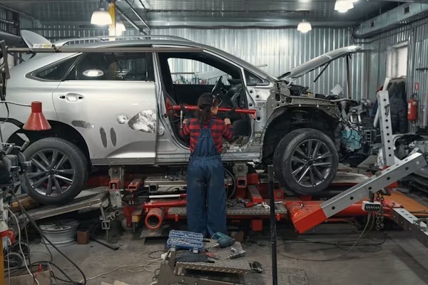 Technician inspecting storm-damaged vehicle at a collision repair shop