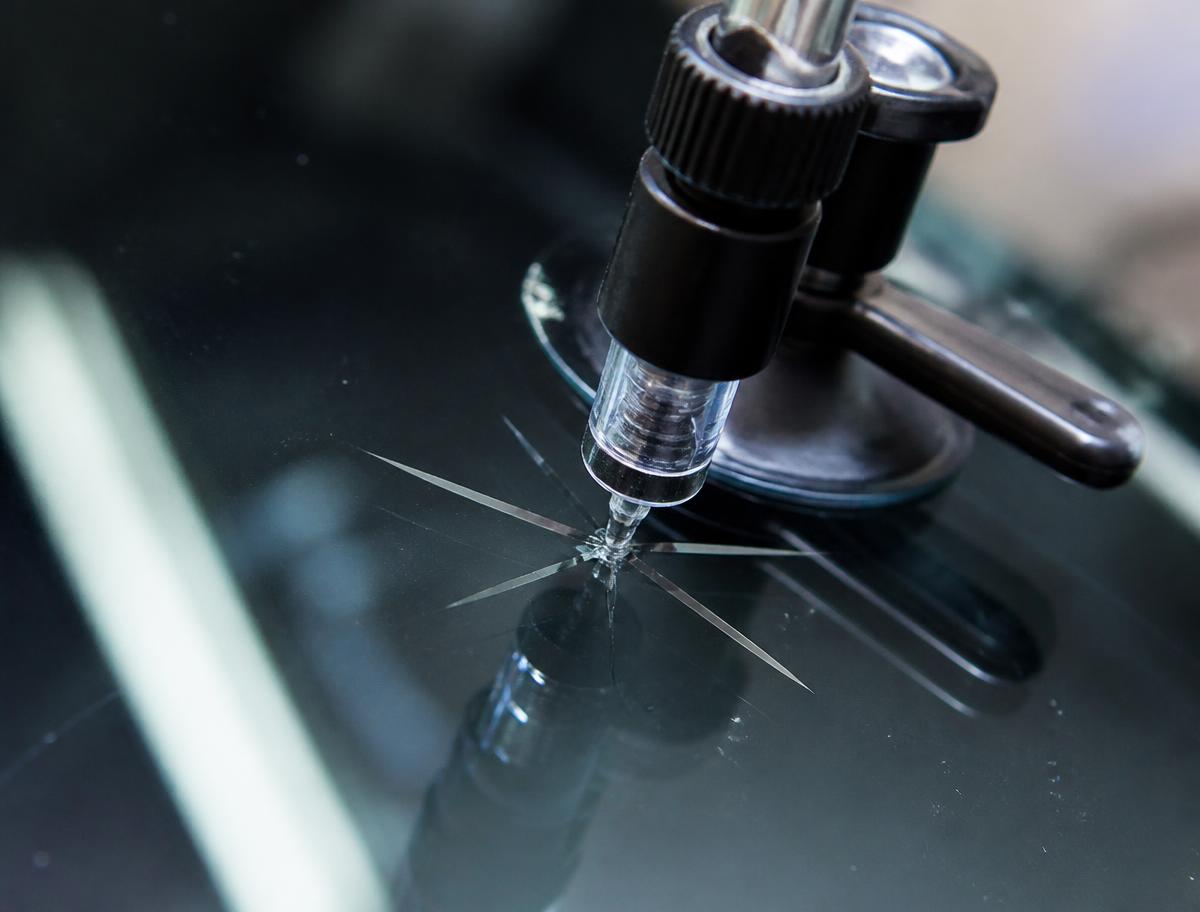 Resin injector filling a rock chip during windshield repair in California